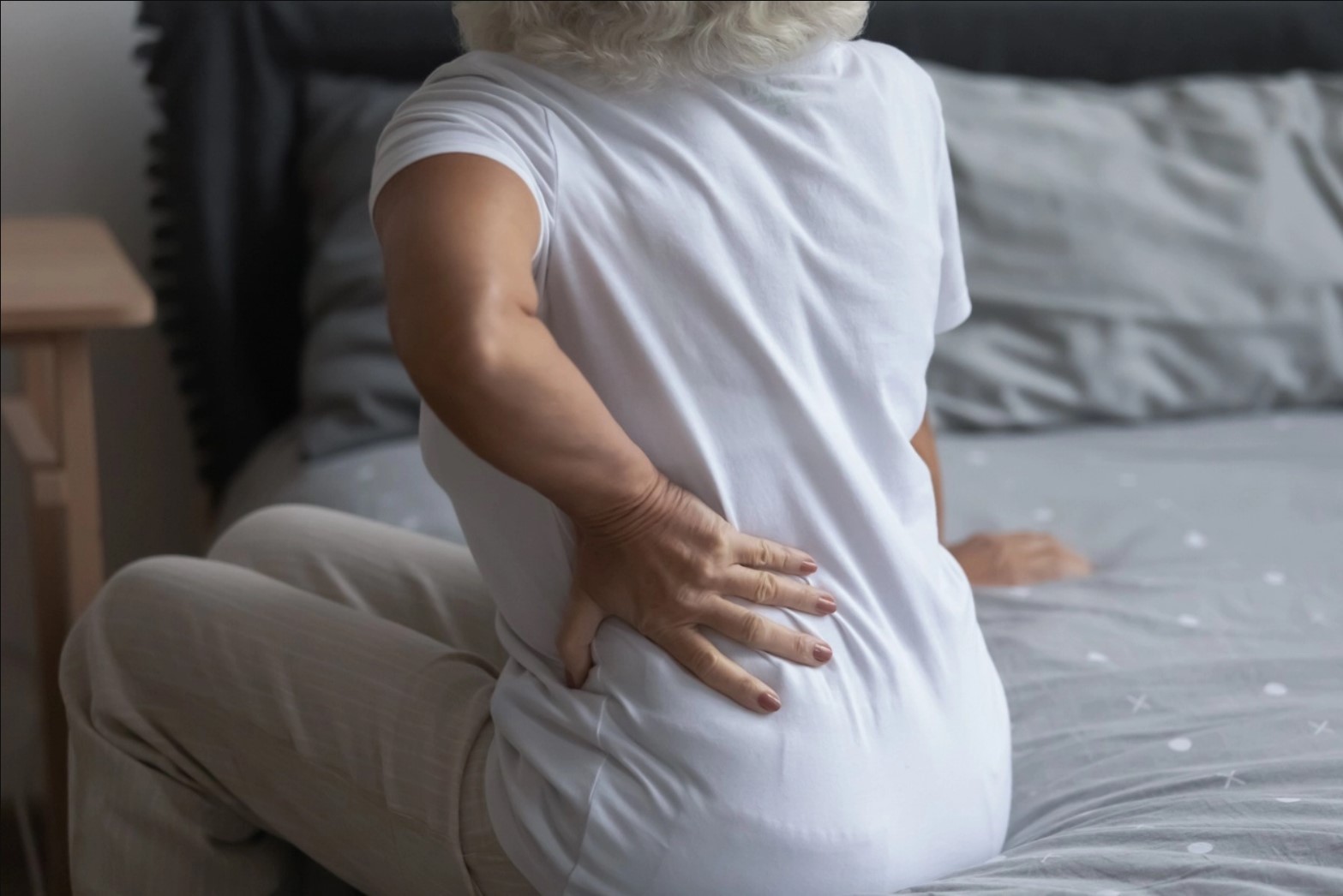 An elderly woman with Sciatica is holding her back with her hand due to back pain.