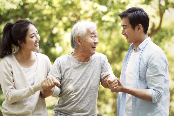 A young couple helping their elderly father stand up from wheelchair.