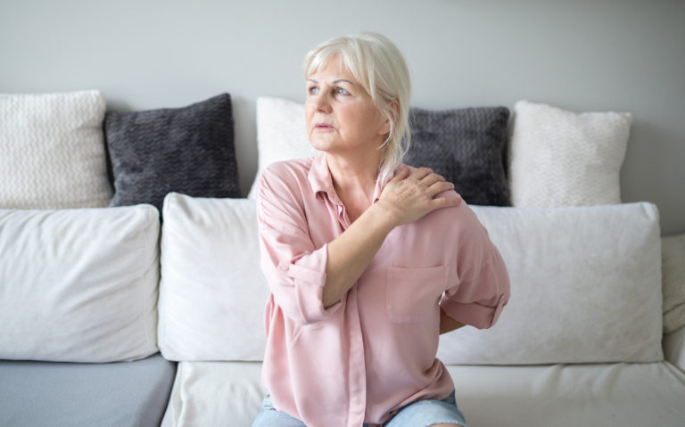 A woman with back pain touching her shoulder and lower back.