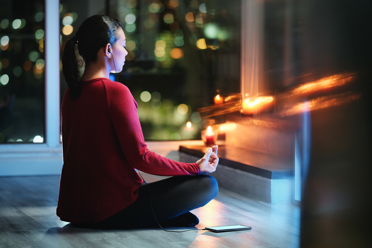 A woman meditating whilst listening to an app for yoga on her phone. She is surrounded by candles.